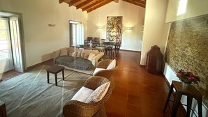 A spacious living area with a high wooden ceiling, a dining table with chairs, a sofa, and a coffee table.