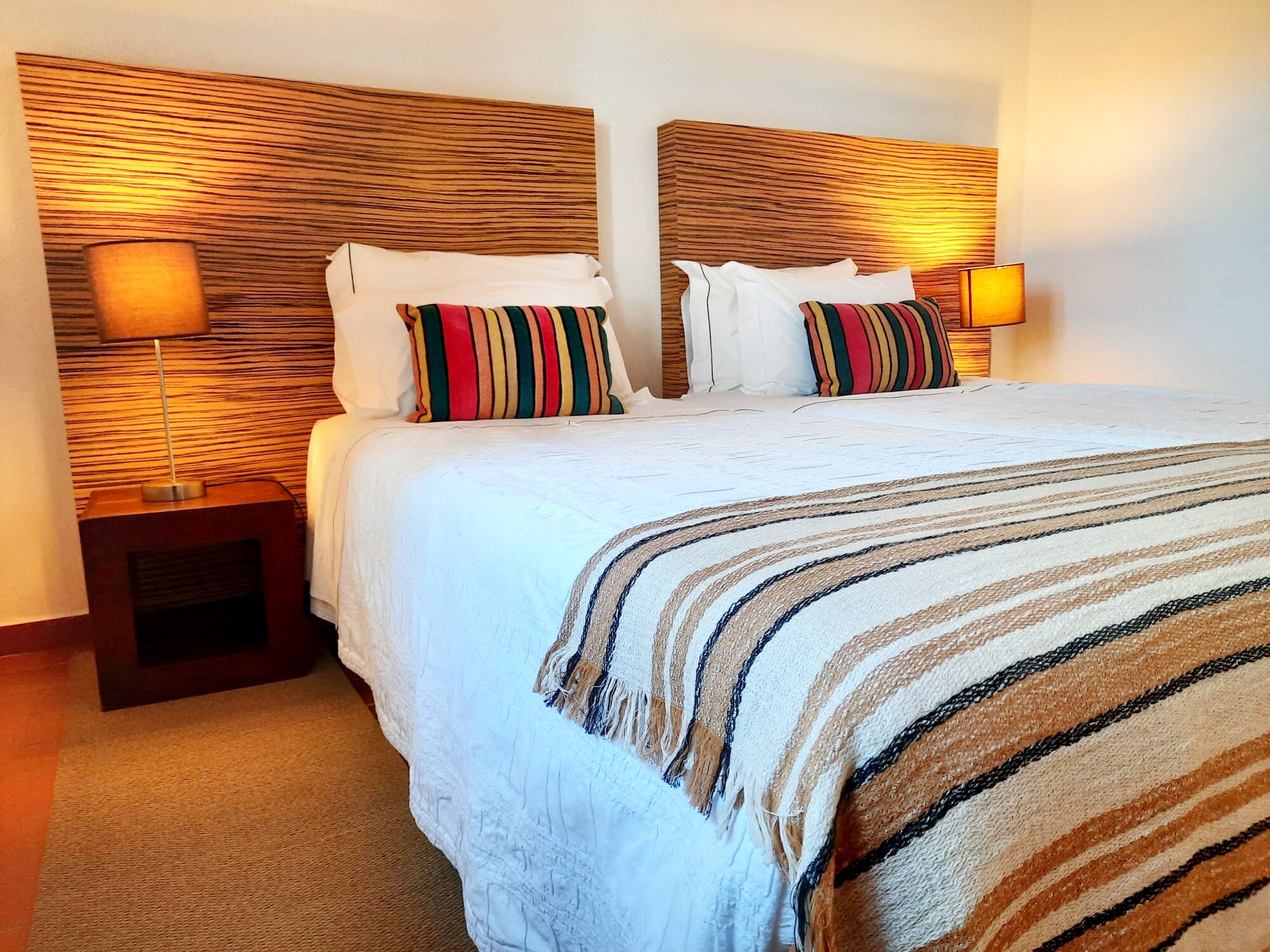 Une chambre d’hôtel avec un grand lit, deux tables de chevet et une tête de lit ornée d’un motif texturé.