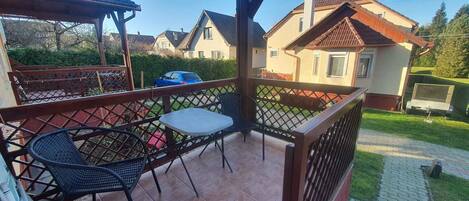 A covered outdoor patio with a table and chairs, surrounded by a wooden fence, with houses in the background.