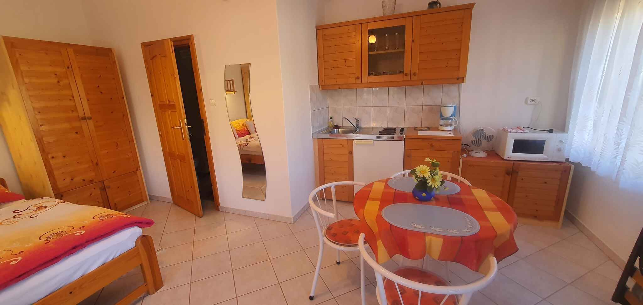 Cocina pequeña con armarios de madera, microondas y un lavamanos. Hay una mesa de comedor con mantel colorido y una silla.