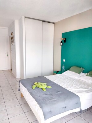 Ein Schlafzimmer mit einem Bett, einer Wand in Türkis, einer grauen Decke und einem grünen Kissen.
