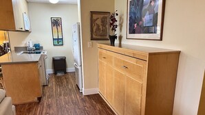 Eine Küche mit Holzausbau, einer Arbeitsplatte und einem Spülbecken. An der Wand befinden sich gerahmte Bilder und ein kleiner Mülleimer.