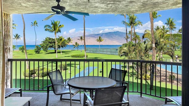 Ein Balkon mit Tisch und Stühlen, der auf einen Golfplatz, Palmen und den Ozean blickt.