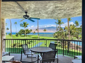 A balcony with a table and chairs, overlooking a golf course, palm trees, and a view of the ocean. - Maui Sunset Vacation Rentals B219 (Kihei)