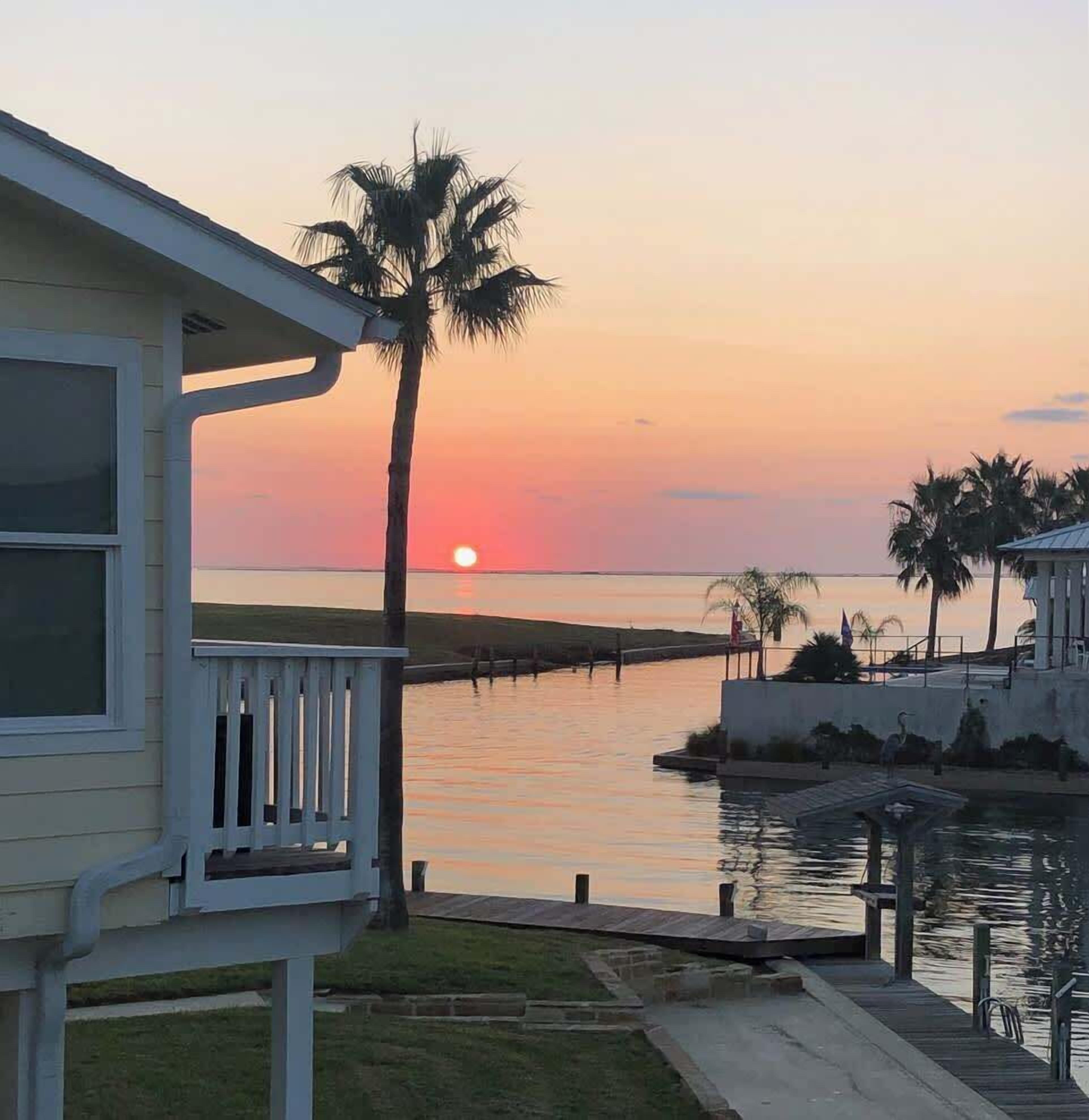 A waterfront property with a deck, a palm tree, and a sunset view.