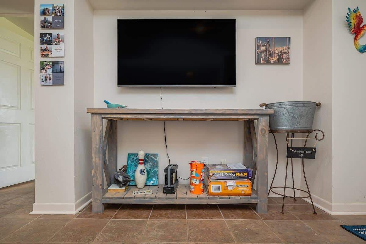 Una sala de estar con un televisor de pantalla plana montado en la pared, un mueble de madera con varios objetos, y un cubo de metal sobre un soporte.