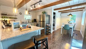 A kitchen with a granite countertop, wooden bar stools, a stainless steel refrigerator, and a dining area with a table and chairs. - 40min from Portland- Sandy Ridge Family Cottage (Oxford)