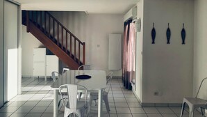 A spacious dining area with a white table and chairs, a staircase leading to another level, and a wall with three decorative fish sculptures.
