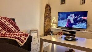 A living room with a television, a couch, a coffee table, and a decorative tree.