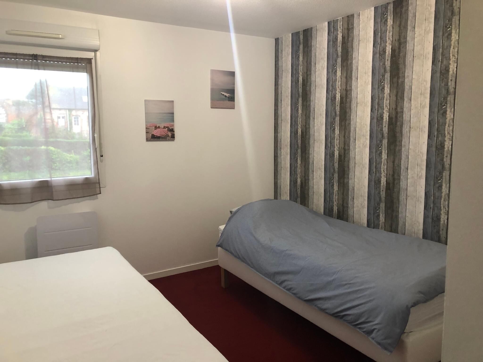 Une petite chambre avec un lit simple, une fenêtre, un radiateur et un mur à rayures.