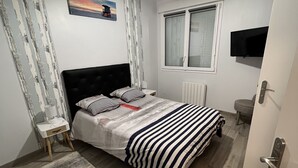 Une chambre à coucher comprenant un lit, une table de chevet, un téléviseur fixé au mur, une fenêtre et une porte.