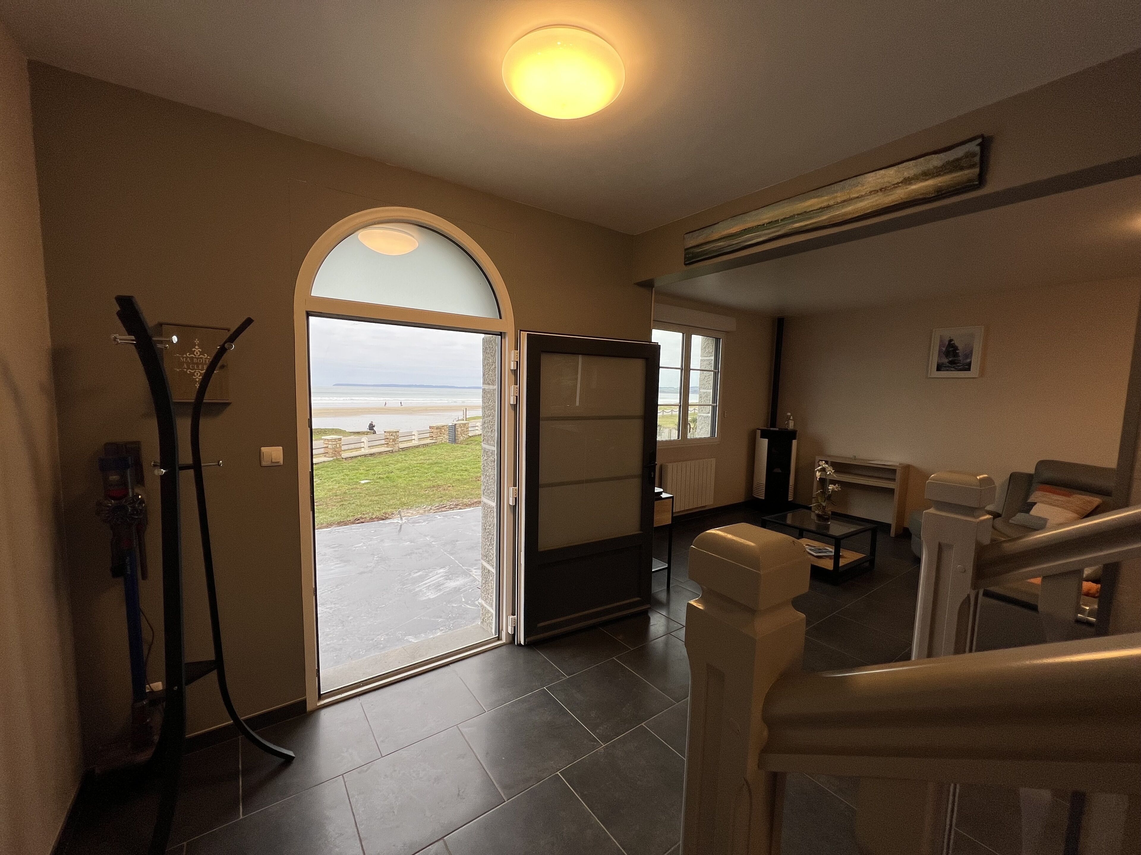 A spacious living area with a large glass door leading to a balcony overlooking a beach.