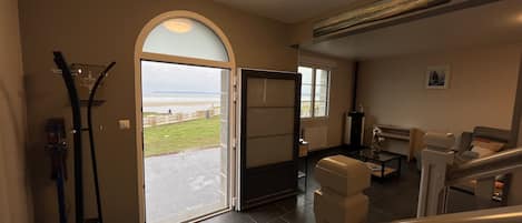 A spacious living area with a large glass door leading to a balcony overlooking a beach.
