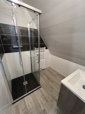 Un baño moderno con ducha de vidrio, lavamanos blanco y piso de madera.
