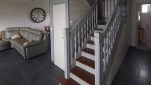 Un salon moderne avec un canapé d’angle gris, une horloge murale blanche et un escalier avec des marches en bois et des rampes blanches.