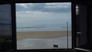 Une vue sur une plage, visible par une fenêtre, avec un panneau indiquant « Pupol de Lestebet ».