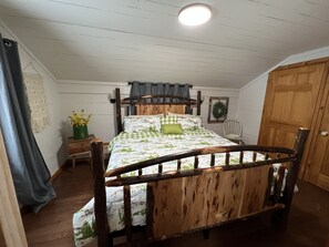 Ein hölzernes Himmelbett mit floralem Überwurf, ein Nachttisch mit Blumenvase, ein weißer Stuhl und ein Holzschrank.