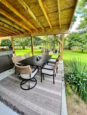 Eine Terrassensitzgruppe im Freien mit Tisch und Stühlen, einem Grill und einem überdachten Bereich mit Blick auf eine grüne Landschaft.