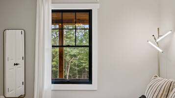 A bedroom with a large window, a bedside table, a lamp, and a wardrobe.