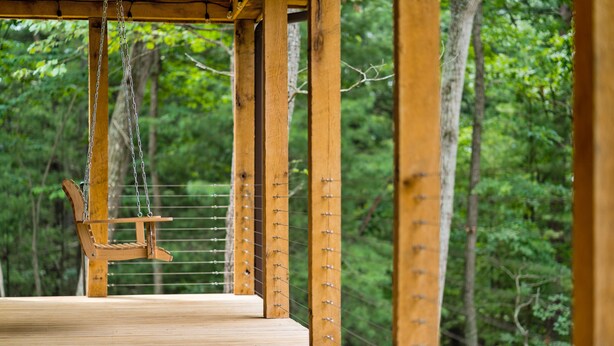 A wooden deck with a swing, surrounded by trees.