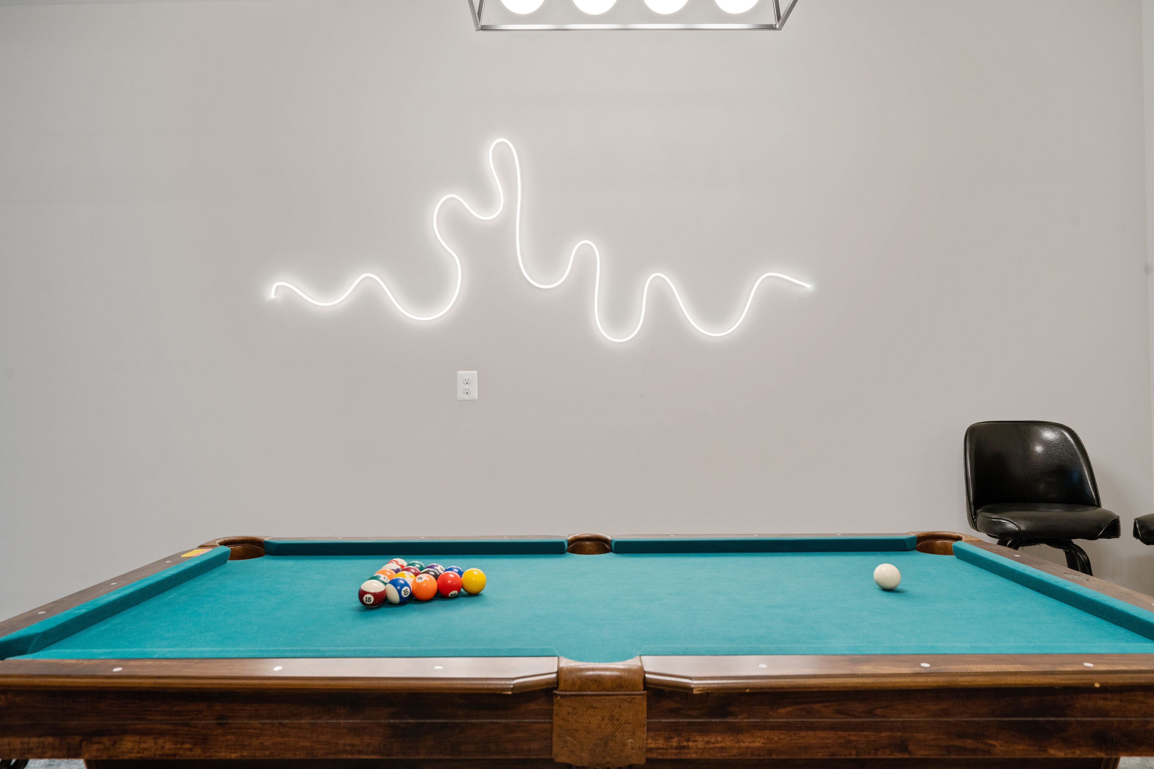 A pool table with balls and a neon light design on the wall.