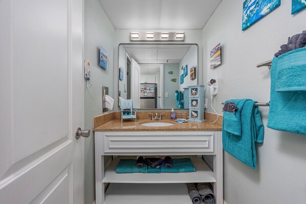 Une salle de bain avec un meuble-lavabo blanc, un évier, un miroir et un porte-serviettes.