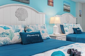 A bedroom with two beds, a white headboard with a seashell design, and a blue and white coral-patterned bedspread. - Harmony’s Ocean Haven-Stunning Oceanfront Views~Pools & Lazy River~Updated! (Myrtle Beach)