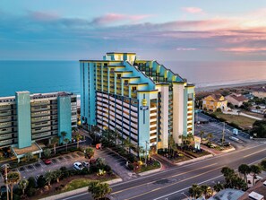 A multi-story hotel with a parking lot and a view of the ocean. - Harmony’s Ocean Haven-Stunning Oceanfront Views~Pools & Lazy River~Updated! (Myrtle Beach)