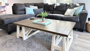Ein modernes Wohnzimmer mit einem dunkelgrauen Ledersofa, einem Holztisch und einem flauschigen, grauen Teppich.
