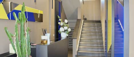 A modern reception area with a reception desk, a staircase, and a cactus plant.