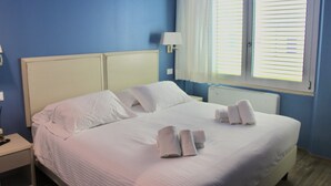 A neatly made bed with white linens and towels, a bedside table with a lamp, and a window with blinds. - Hotel Gabbani  (Bibbona)