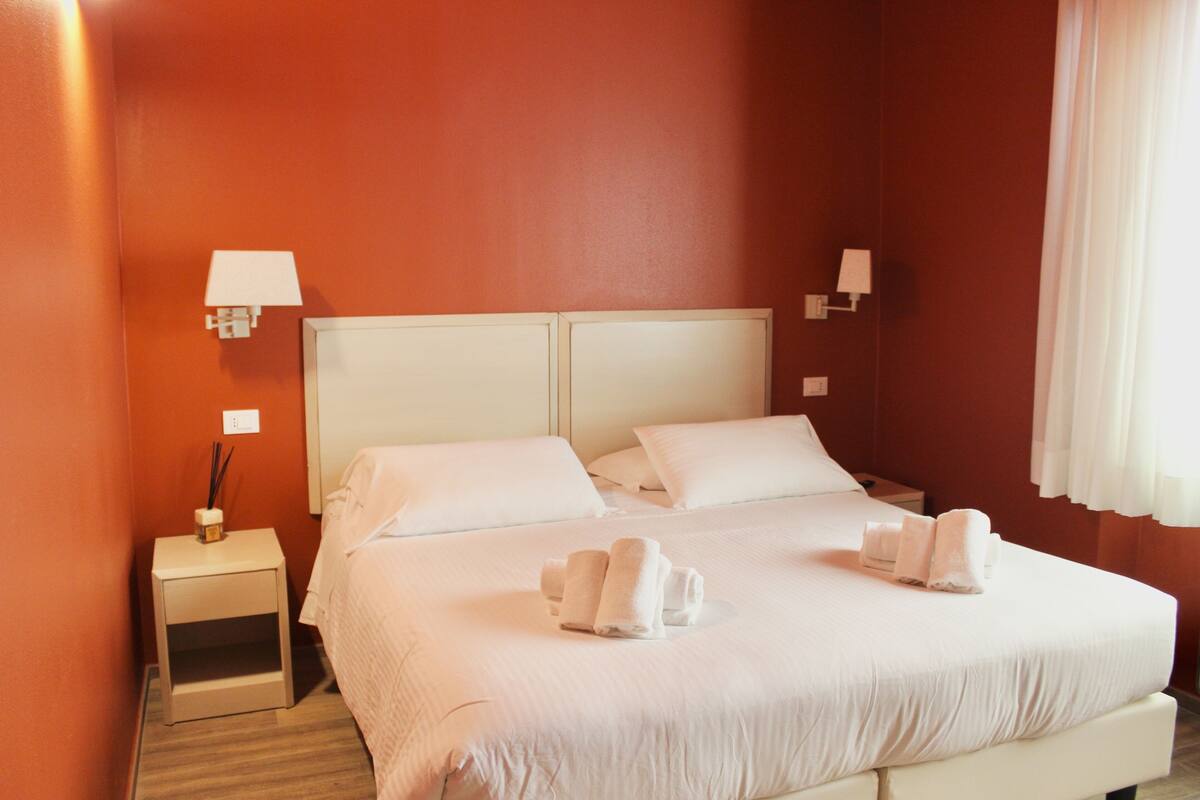 A hotel room with a large bed, two bedside tables, and two wall-mounted lamps.