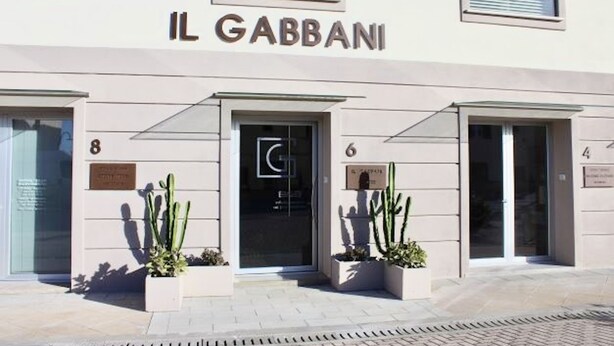 A building with the sign 'IL GABBANI' above the entrance. There are three numbered doors, 8, 6, and 4, and two potted plants on the sidewalk. - Hotel Gabbani  (Bibbona)
