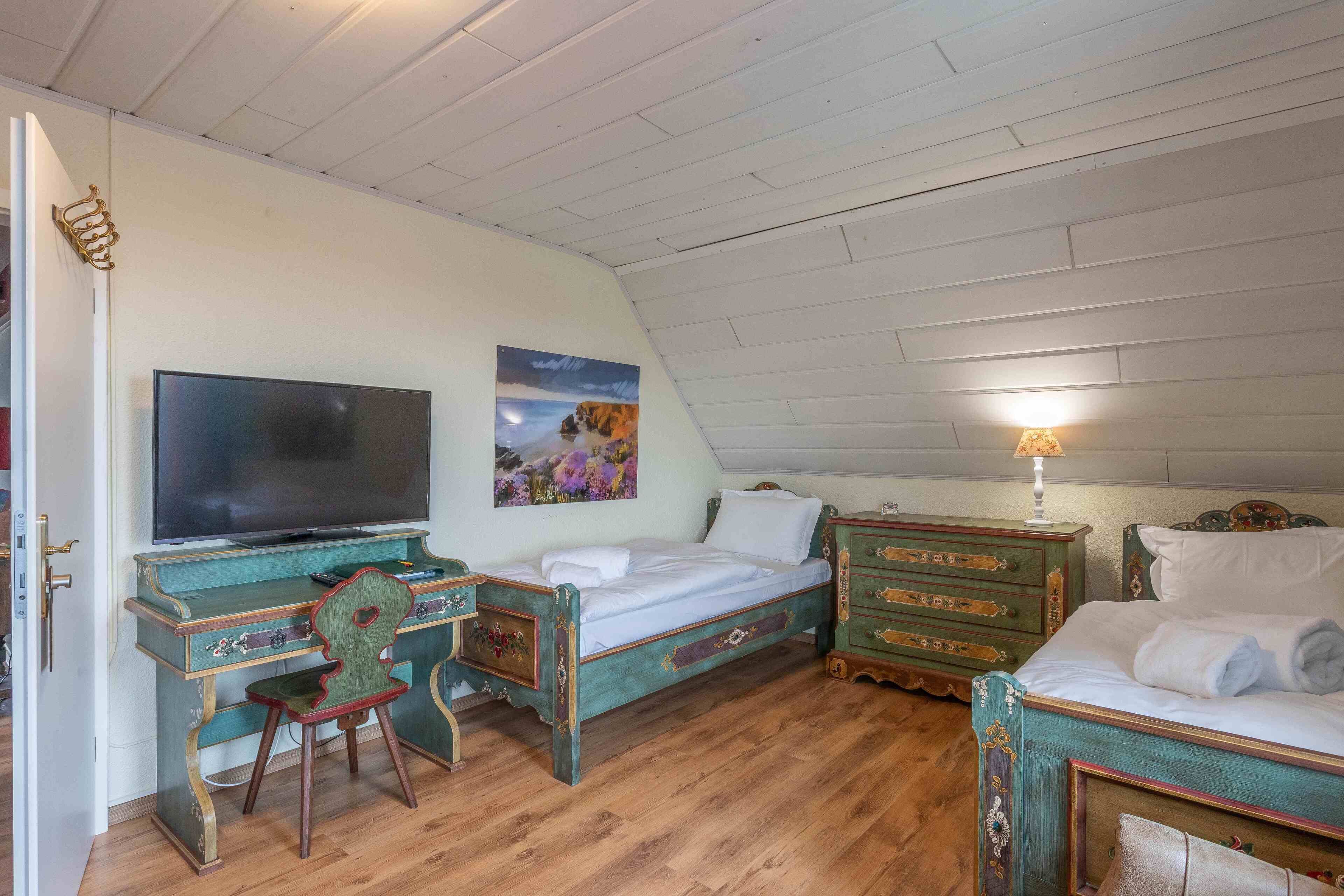Ein Zimmer mit einem Bett, einem Schreibtisch mit Fernseher, einem Sessel, einer Kommode und einem Bild an der Wand.