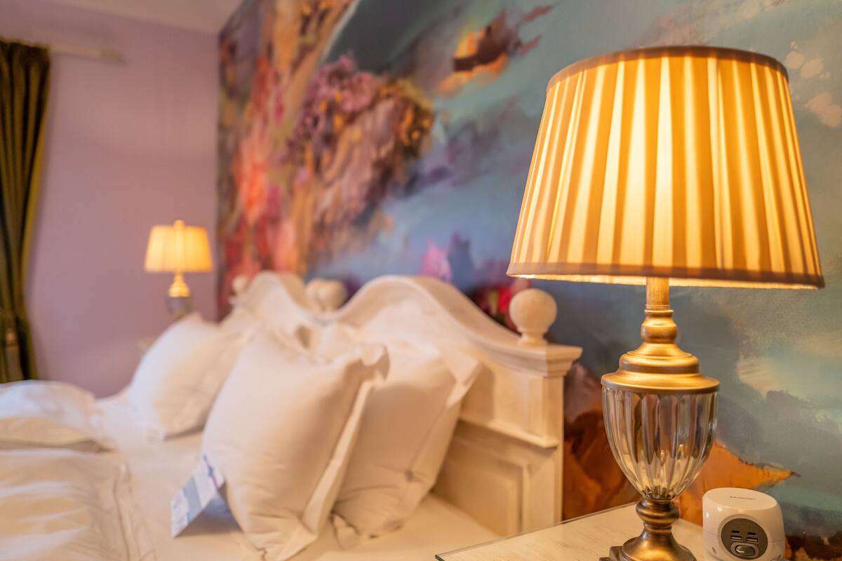 A hotel room with a bed, a lamp, and a painting on the wall.