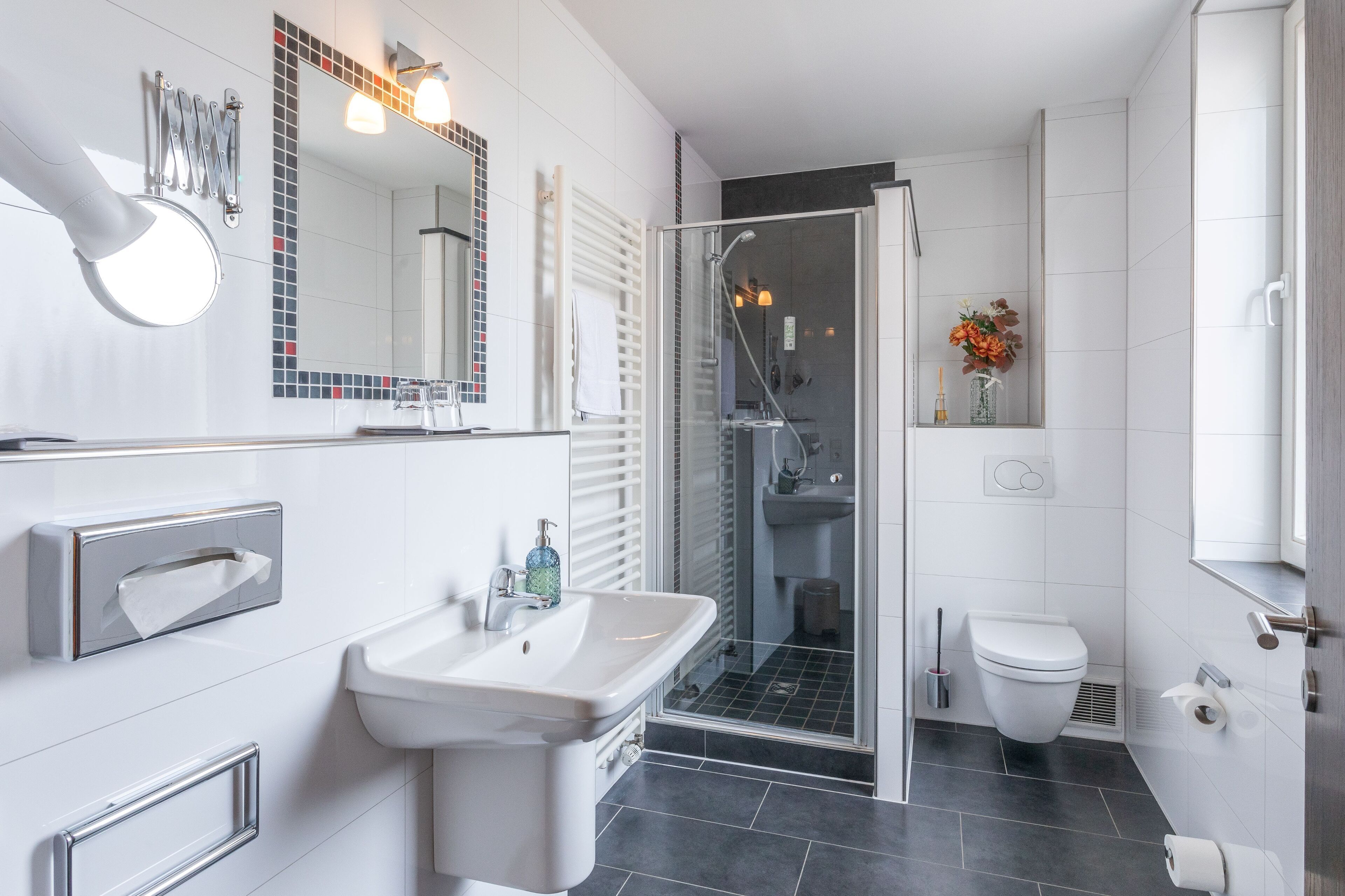 Un baño moderno con ducha de vidrio, un lavamanos blanco y un inodoro.