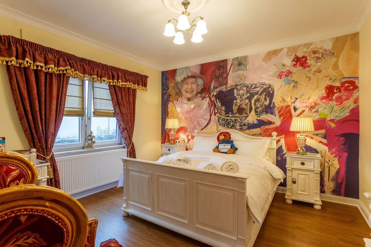 A bedroom with a large bed, a nightstand, a chair, and a window with curtains.