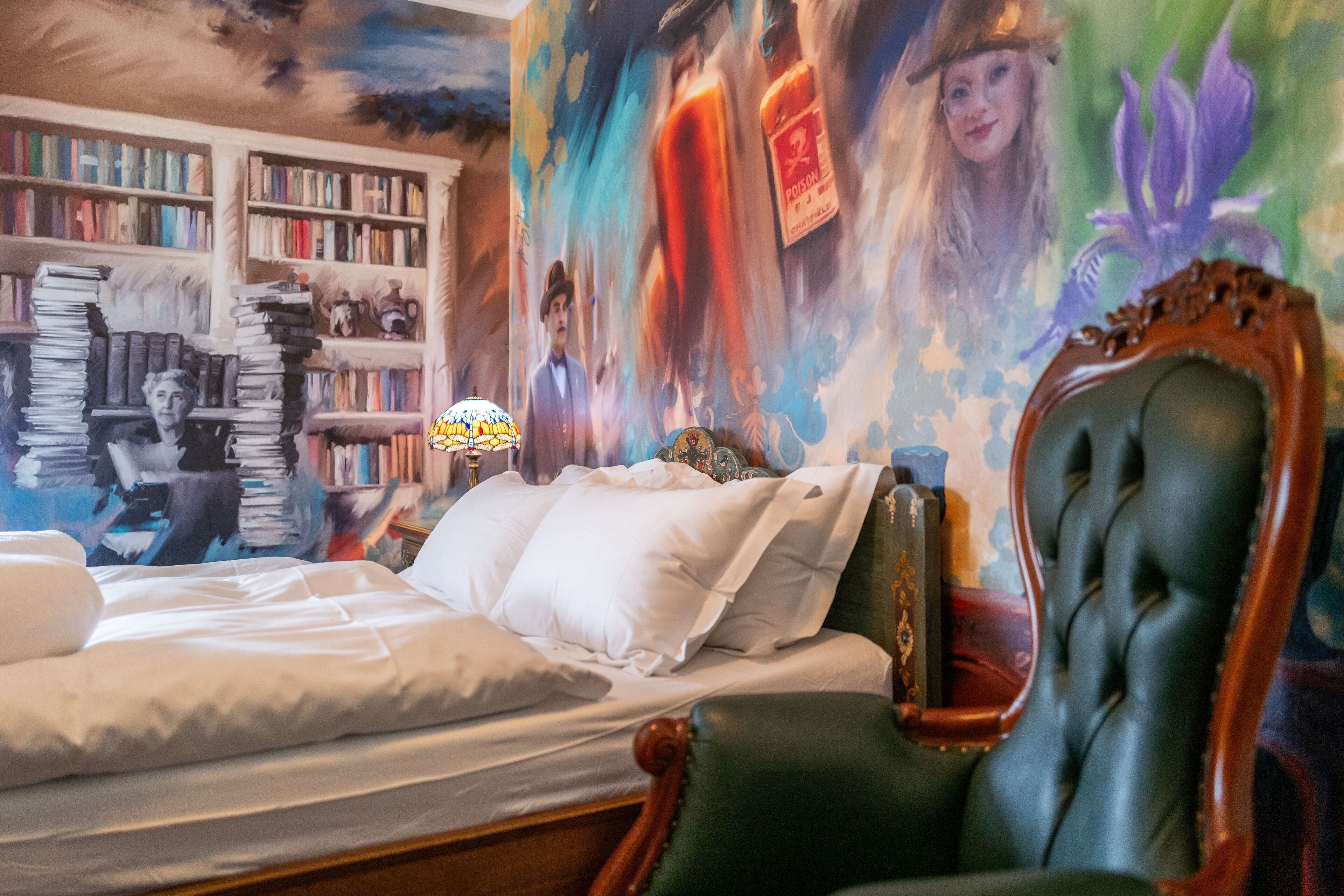 Quarto com uma cama grande, uma poltrona verde, uma estante e um mural na parede.