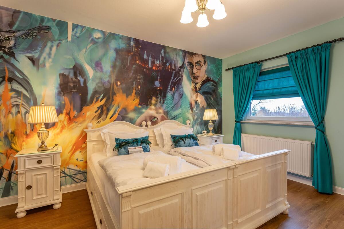 A bedroom with a large wall mural, a white bed, teal curtains, and two bedside lamps.