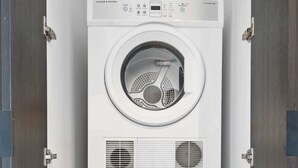 En kombinerad tvätt- och torkmaskin med staplad konstruktion och kontrollpaneler, inbyggd i ett skåp med metallram.