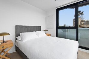A bedroom with a bed, two bedside tables, a window, and a cityscape view.