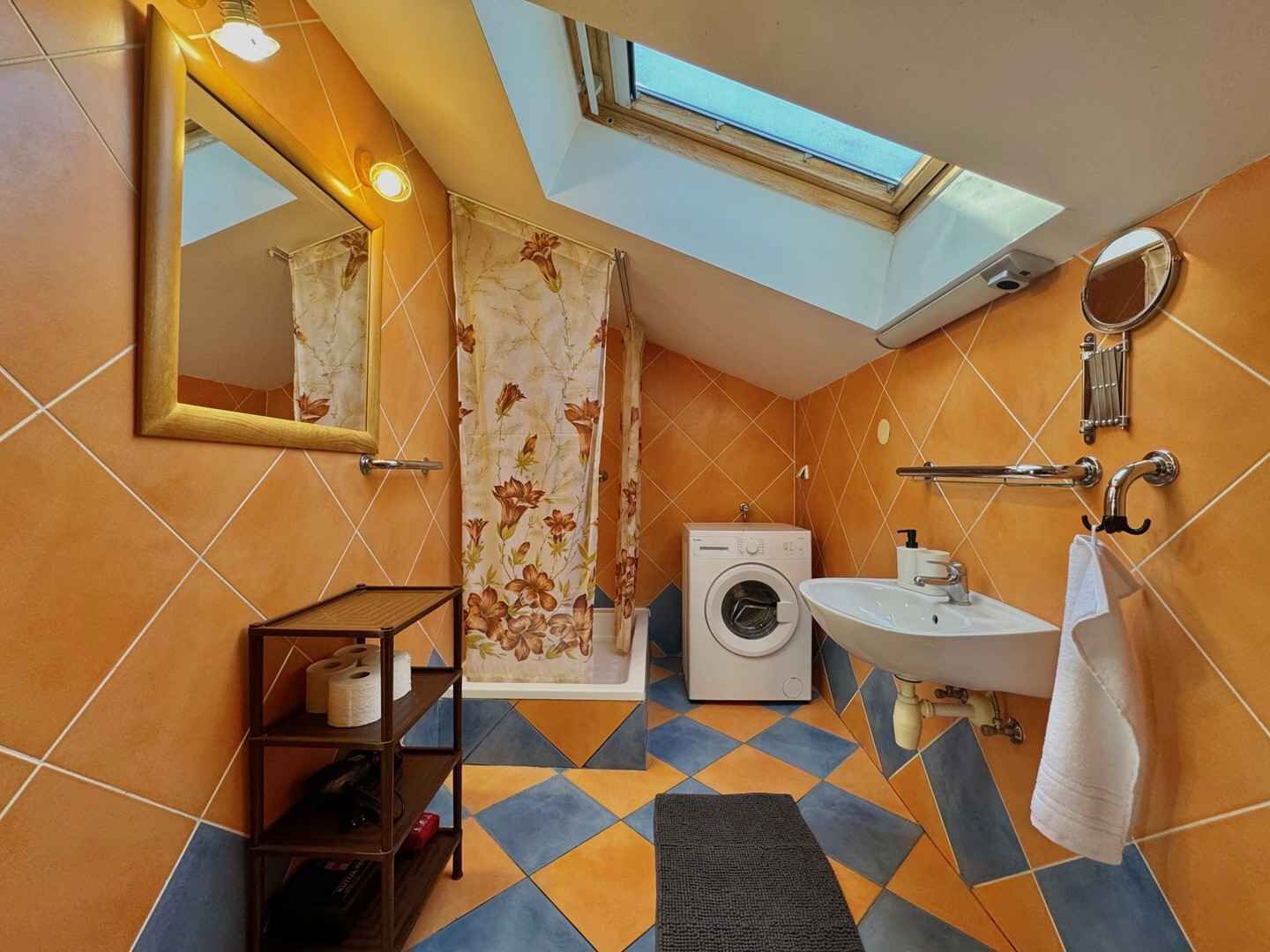 A compact bathroom with a skylight, a washing machine, a sink, and a mirror.