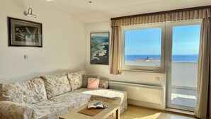 Een woonkamer met een bank, een tafel en uitzicht op de zee door een groot raam.