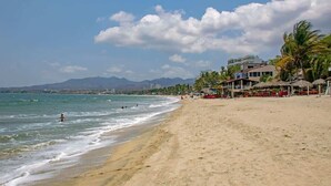 A beach with a sandy shore, ocean waves, and a resort area with buildings and palm trees. - Golden Zone Studio w/ Pool - 2 Min to Beach (Bucerías)