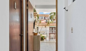 A corridor leading to a balcony with a tiled roof, outdoor furniture, and potted plants.