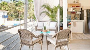 A balcony with wicker furniture, a table with a cactus, and a kitchen area with a refrigerator. - Golden Zone Studio w/ Pool - 2 Min to Beach (Bucerías)