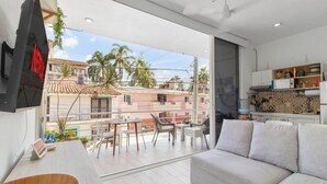 A modern living room with a balcony, a sofa, a dining table, and a kitchen area with cabinets and a water dispenser. - Golden Zone Studio w/ Pool - 2 Min to Beach (Bucerías)