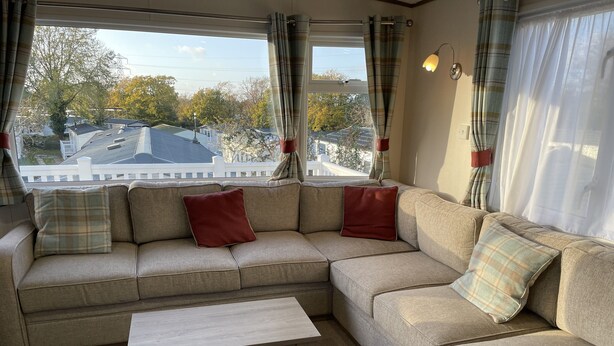 Un salon avec un canapé d’angle beige, une table basse en bois et une vue sur le quartier, grâce à de grandes fenêtres.