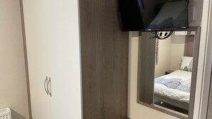 Une chambre à coucher comprenant un lit, une armoire, un miroir et un téléviseur fixé au mur.
