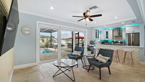A spacious living area with a sliding glass door leading to a pool, a modern kitchen with stainless steel appliances, and a ceiling fan.